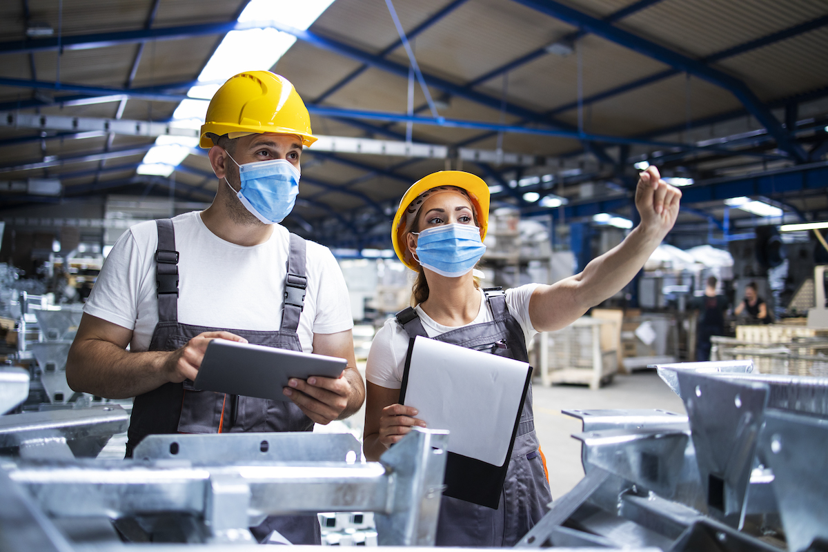 Factory workers with face masks protected against corona virus doing quality control of production in factory. Factory workers with face masks protected against corona virus doing quality control of production in factory.
